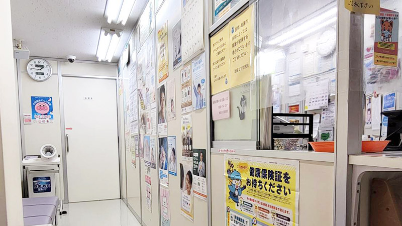 池袋2丁目医院の受付カウンターと廊下。壁には掲示物が多く並び、清潔感のある院内。