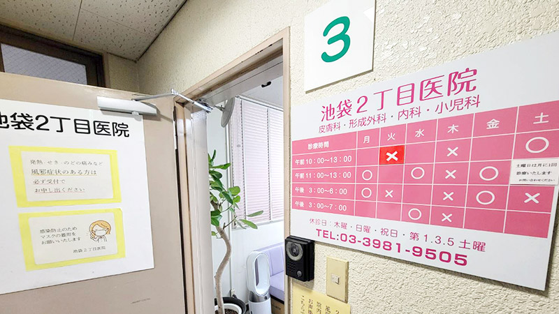 池袋2丁目医院の外観とピンク色の診療時間ボード。医院の診療スケジュールが記載されている。