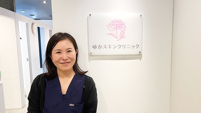 ゆかスキンクリニックの院長・青木由佳先生。白衣姿で穏やかに微笑む立ち姿。